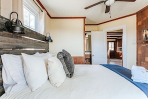 Een slaapkamer met een groot bed, een plafondventilator, een houten hoofdeinde en uitzicht op een andere kamer.