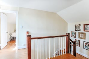 Eine Treppe mit Holzwangen und weißen Spindeln, die zu einem Zimmer mit einem Bett und einem Schreibtisch führt.