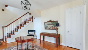 Una escalera con barandillas de madera y un tapete estampado en una habitación con una puerta blanca, una mesita y un cuadro en la pared.
