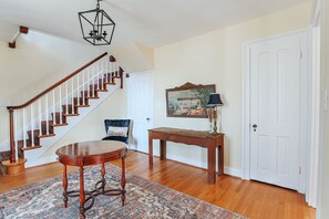 A staircase with wooden railings and a patterned rug in a room with a white door, a small table, and a painting on the wall. - The Farmhouse at Wellington: Waynesboro, Sleeps 12 (Waynesboro)