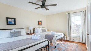 Una habitación de hotel con dos camas, un ventilador de techo, una ventana con cortinas y una alfombra estampada.