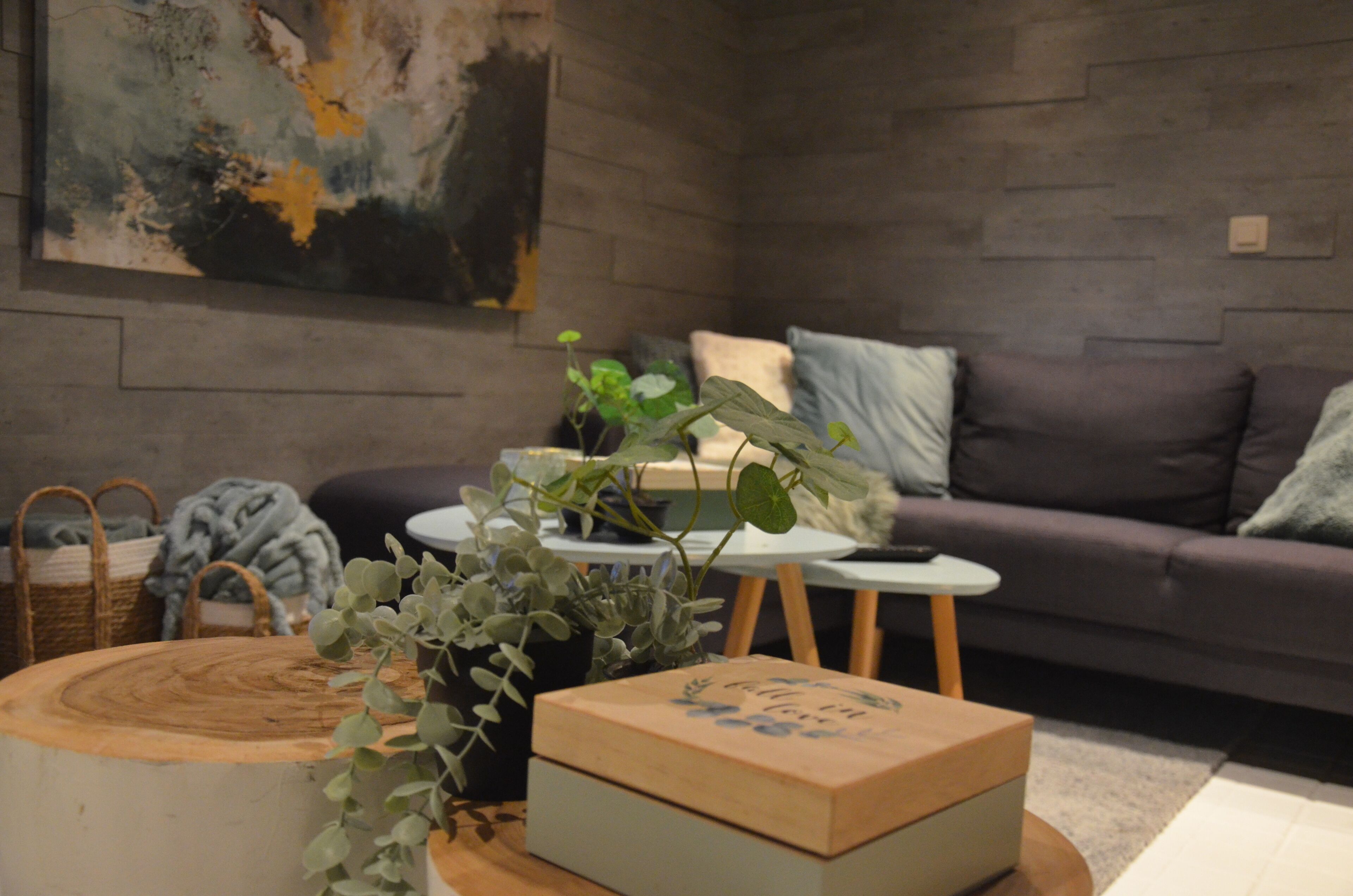 Una sala de estar moderna con un sofá gris, una mesa redonda de madera, una mesita blanca y una planta en maceta.