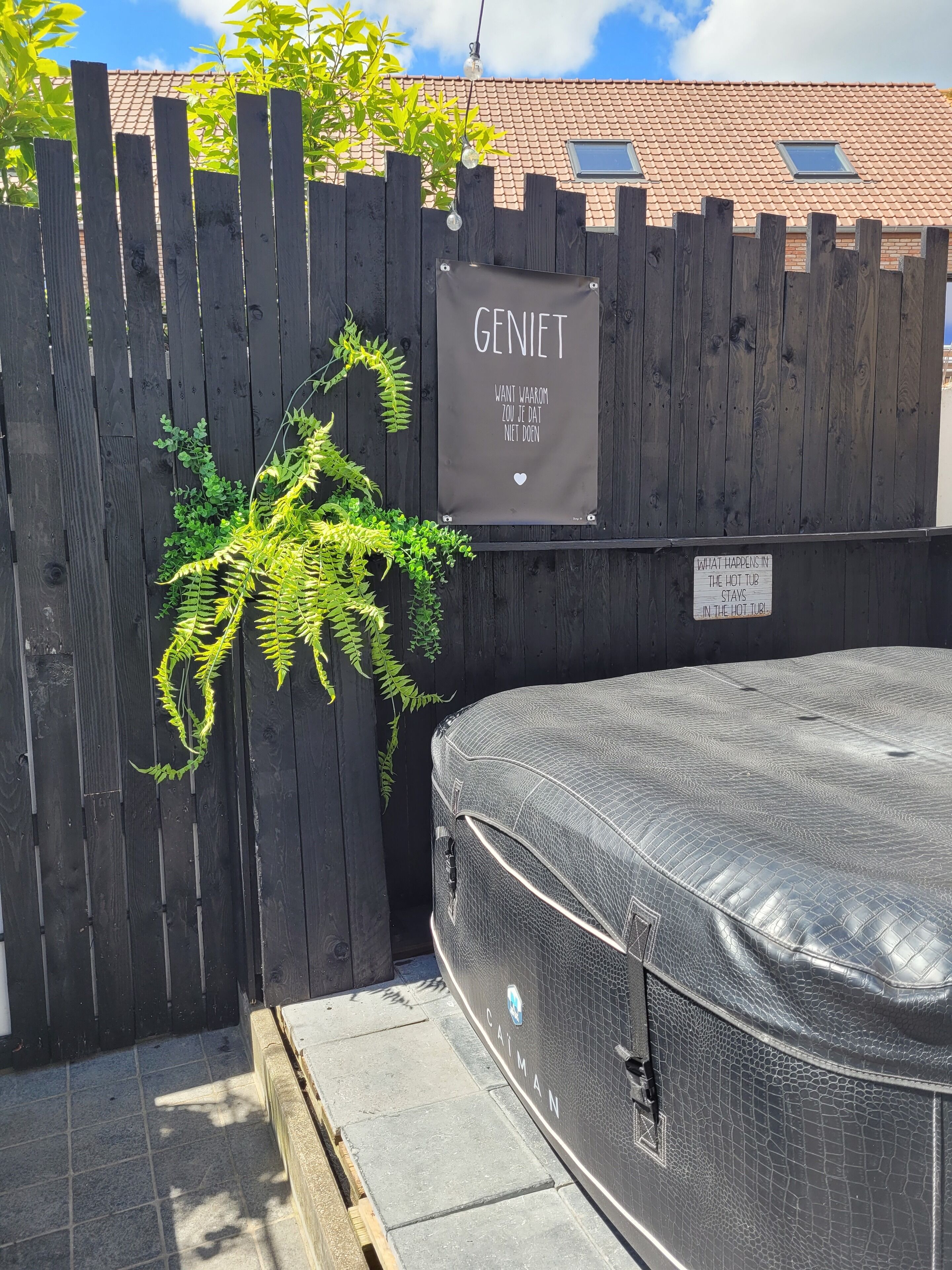 A hot tub area with a wooden fence, a sign reading "GENIET," and a sign stating "WHAT HAPPENS IN THE HOT TUB STAYS IN THE HOT TUB."