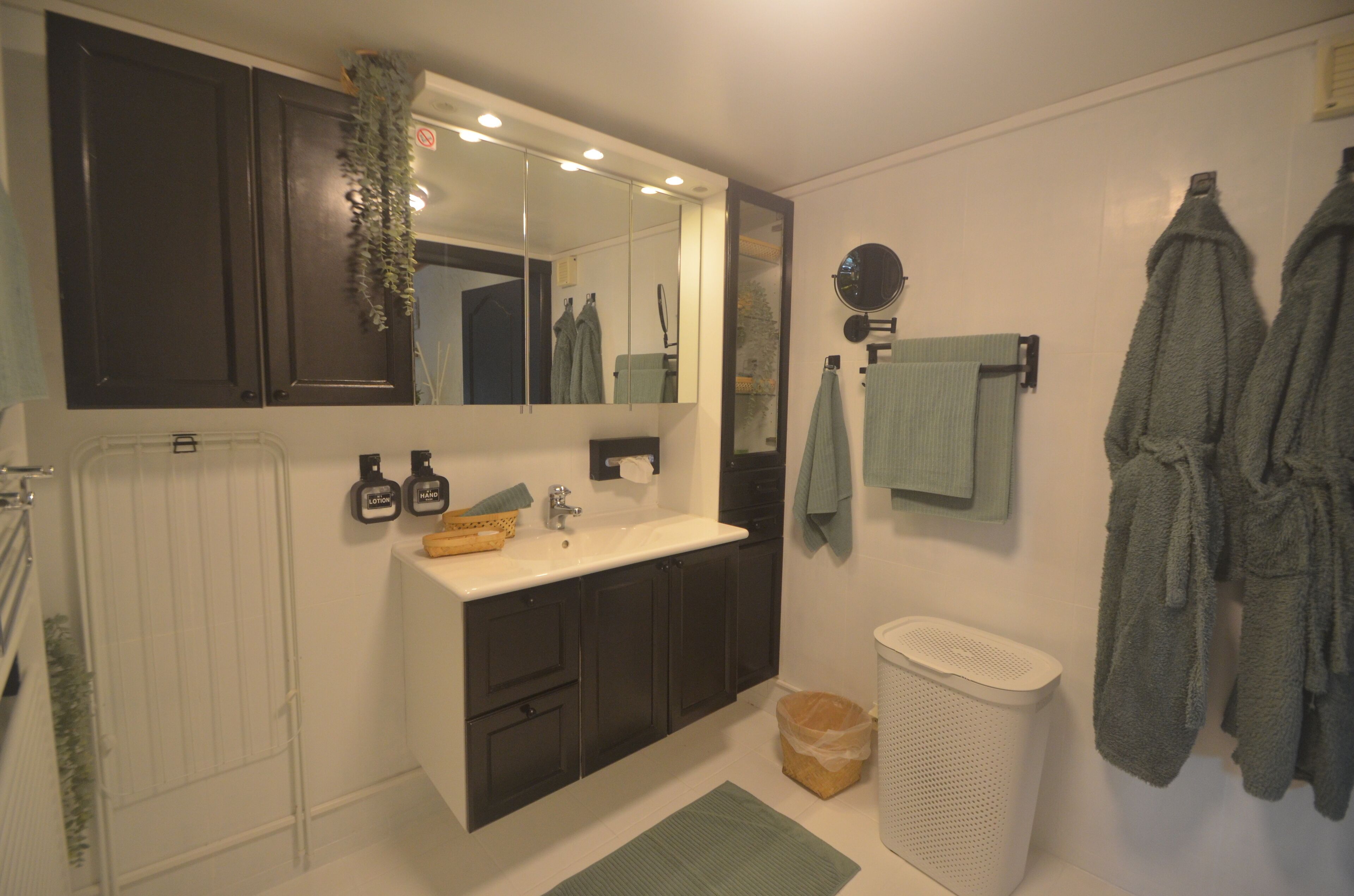 A bathroom with a sink, mirror, towel rack, and a trash bin.
