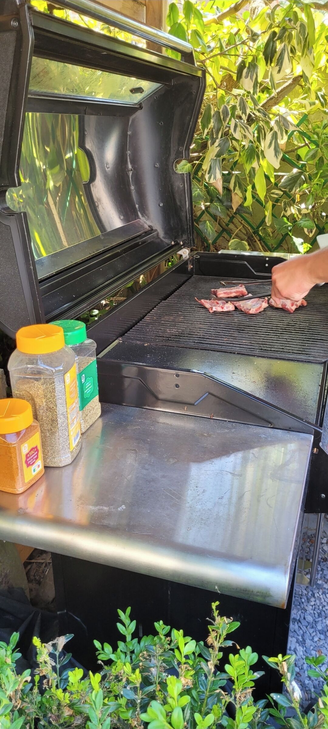 Un barbecue ouvert avec de la viande, des condiments et une personne qui fait griller la viande.