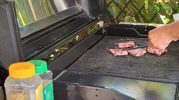 An open grill with meat, condiments, and a person grilling.