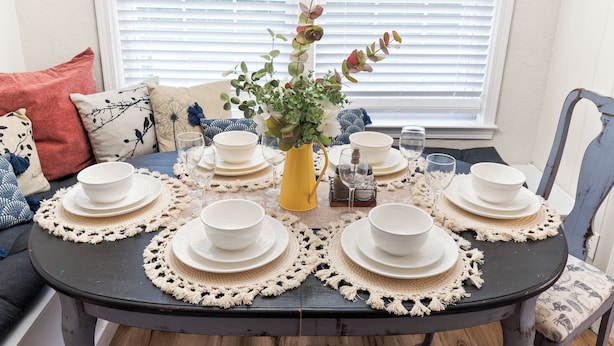 A dining table set with white plates, bowls, and a yellow vase with flowers, surrounded by a crocheted table runner. - 3 Queen Beds, 2 min to Fairgrounds, Fenced Yard (Perry)