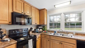 A kitchen with wooden cabinets, a black stove, a microwave, a sink, and a window with a view of the backyard. - 3 Queen Beds, 2 min to Fairgrounds, Fenced Yard (Perry)