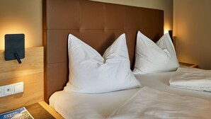 A hotel room with a brown headboard, white pillows, and a bedside table with a magazine.