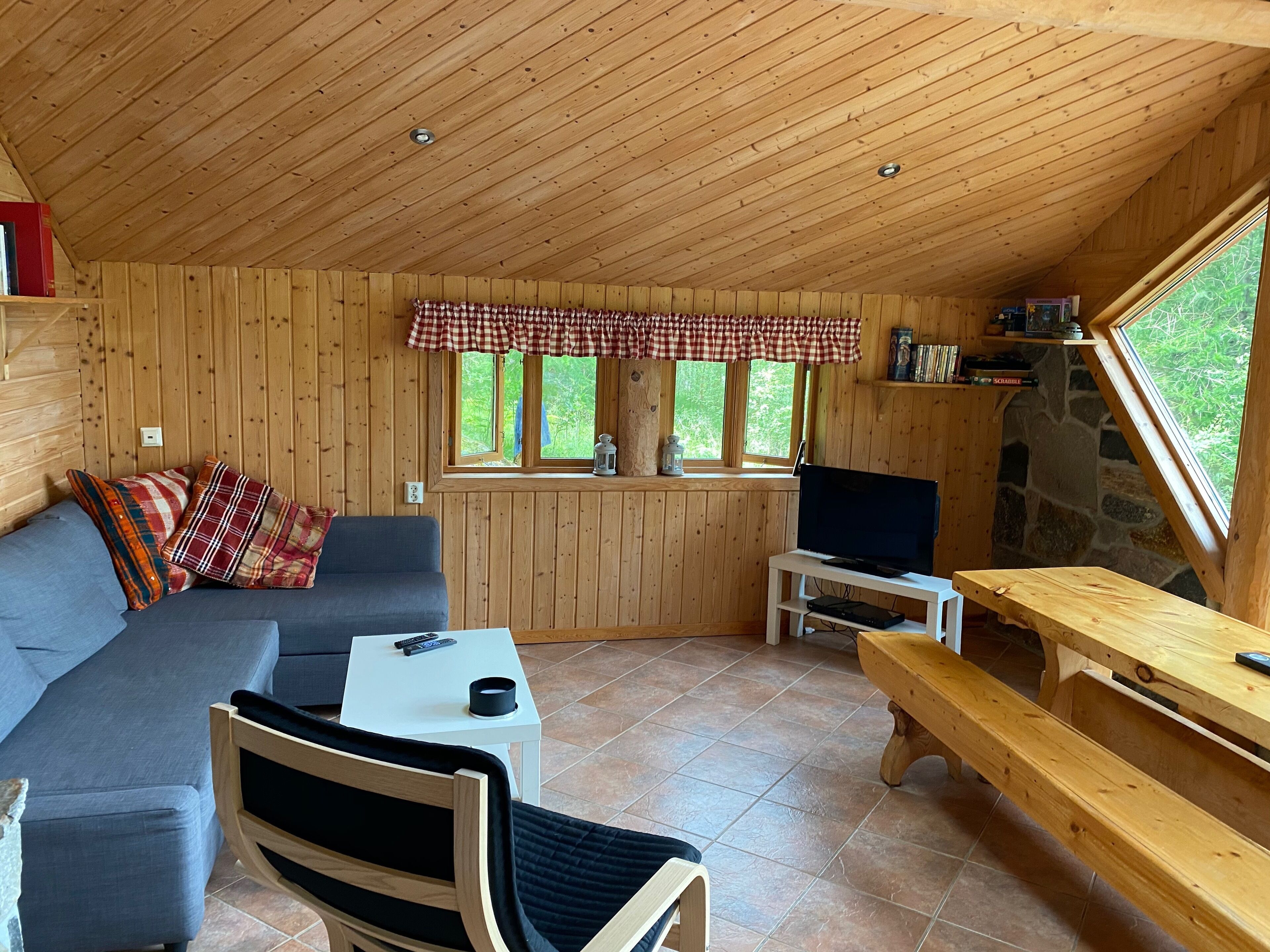 A cozy cabin interior with a wooden ceiling, a sofa, a bench, a table, and a TV.