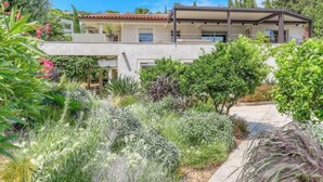 A modern house with a covered patio, surrounded by lush greenery and a clear blue sky. - Designer house with swimming pool, 6 people, 300 m from the center (Le Lavandou)