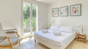 A bedroom with a large bed, a chair, and a window with a view of greenery. - Designer house with swimming pool, 6 people, 300 m from the center (Le Lavandou)
