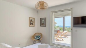 A bedroom with a bed, a chair, a television, and a view of the outside. - Designer house with swimming pool, 6 people, 300 m from the center (Le Lavandou)