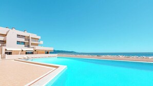 Un hotel moderno con una gran piscina, vistas a la playa y un cielo azul despejado.