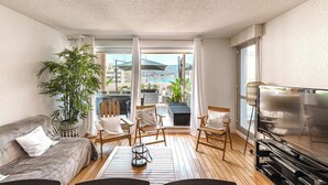 Un salón con sofá, sillas, televisor y un amplio ventanal con vista a una piscina.