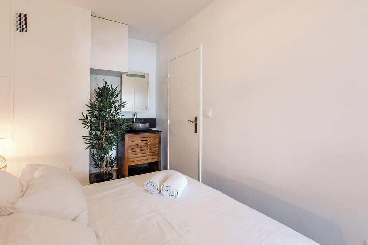 A hotel room with a bed, a wooden dresser, a potted plant, and a white door.