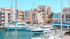 Un puerto deportivo con varios yates amarrados, rodeado de edificios de varios pisos con balcones y un restaurante llamado "LA BRASSERIE DU PORT".