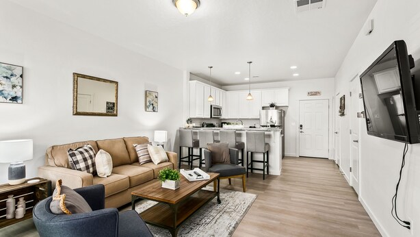 A modern living room with a sofa, coffee table, and TV. A kitchen is visible in the background with a sign reading "KITCHEN".