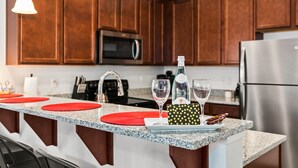 A kitchen with wooden cabinets, a stainless steel refrigerator, a microwave, and a granite countertop.