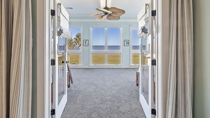 A hallway leading to a balcony with a view of the ocean, a ceiling fan, and a carpeted floor. - STUNNING Oceanfront Home! Golf & Ocean Views, Hot Tub, Golf Cart, Pool Access! (Isle Of Palms)
