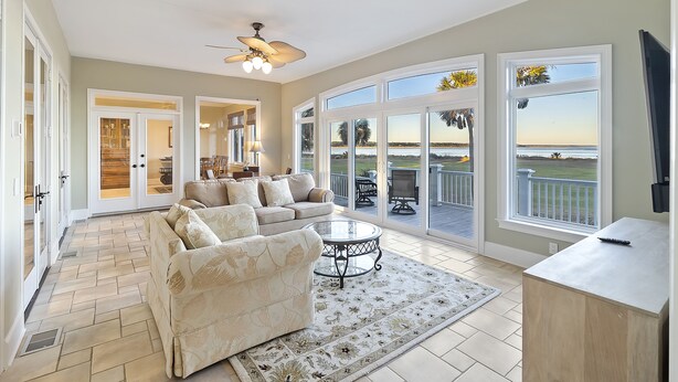 A spacious living room with a large window, a ceiling fan, and a view of the outdoors. - STUNNING Oceanfront Home! Golf & Ocean Views, Hot Tub, Golf Cart, Pool Access! (Isle Of Palms)