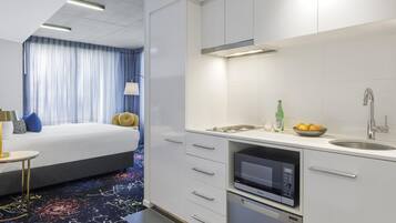 Una habitación de hotel moderna con una cama, una pequeña zona de estar, una kitchenette y un baño.