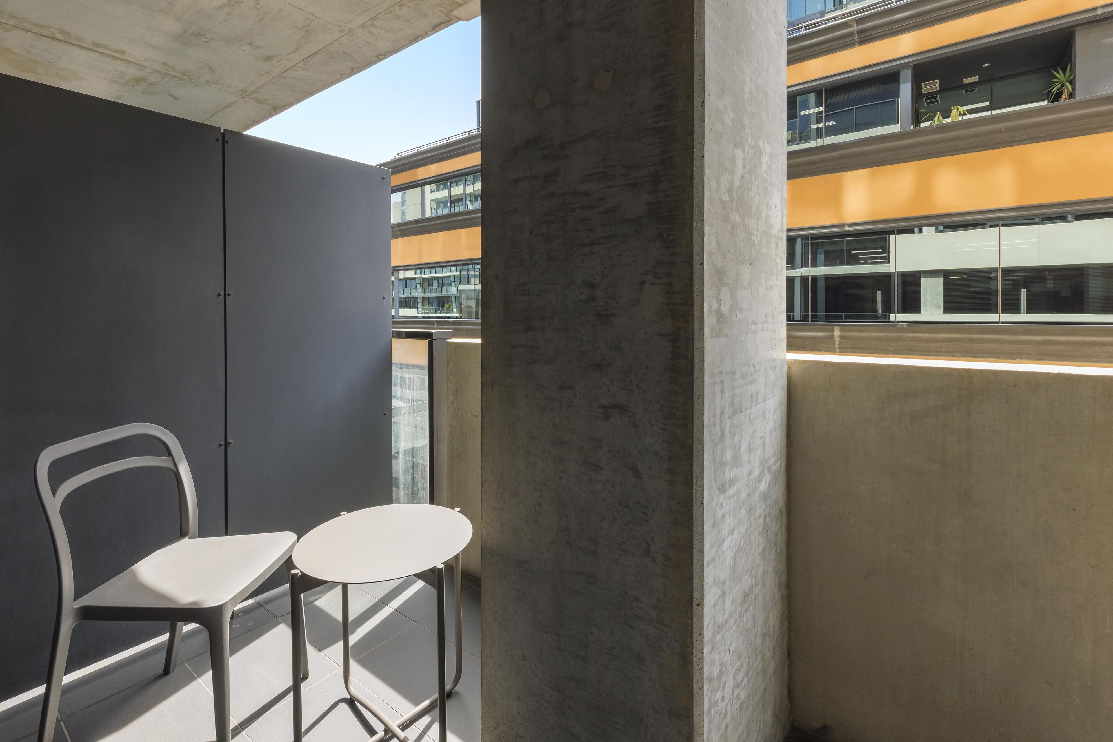 A balcony with two white chairs and a concrete pillar.