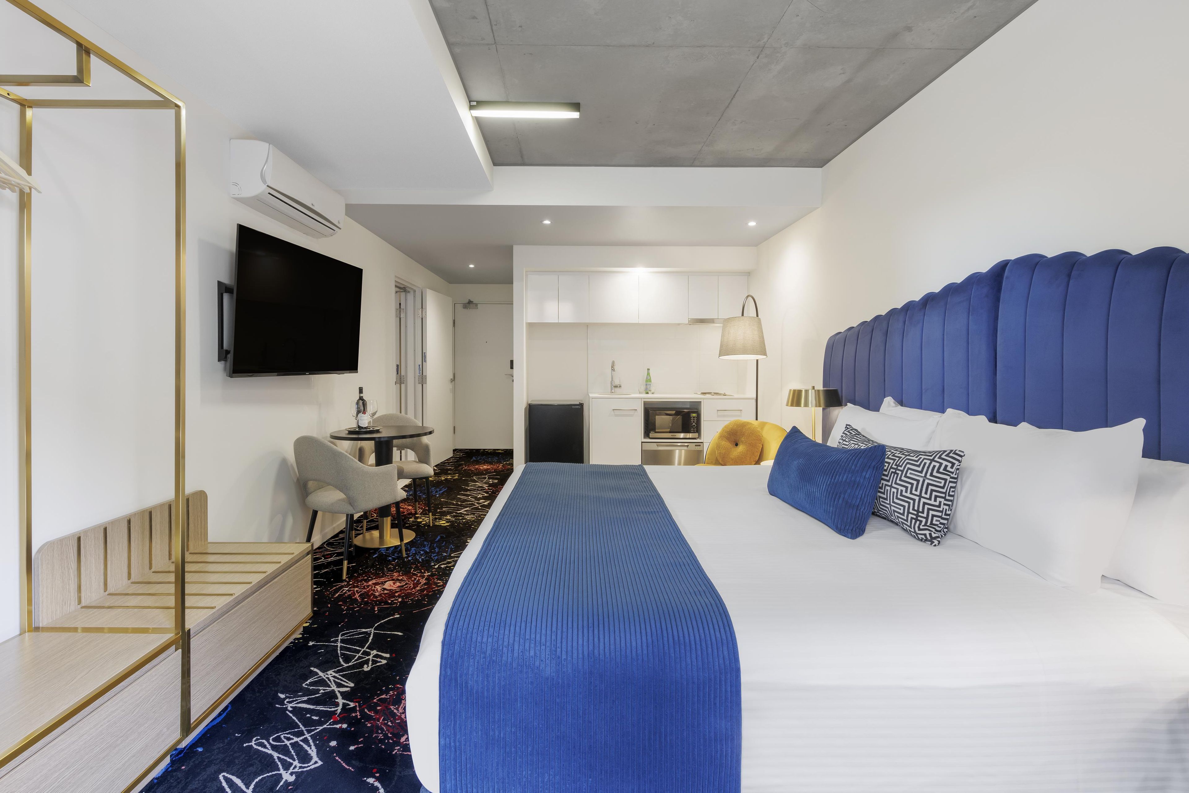 Una habitación de hotel moderna con una cama grande, un televisor de pantalla plana, una zona de comedor y una kitchenette.