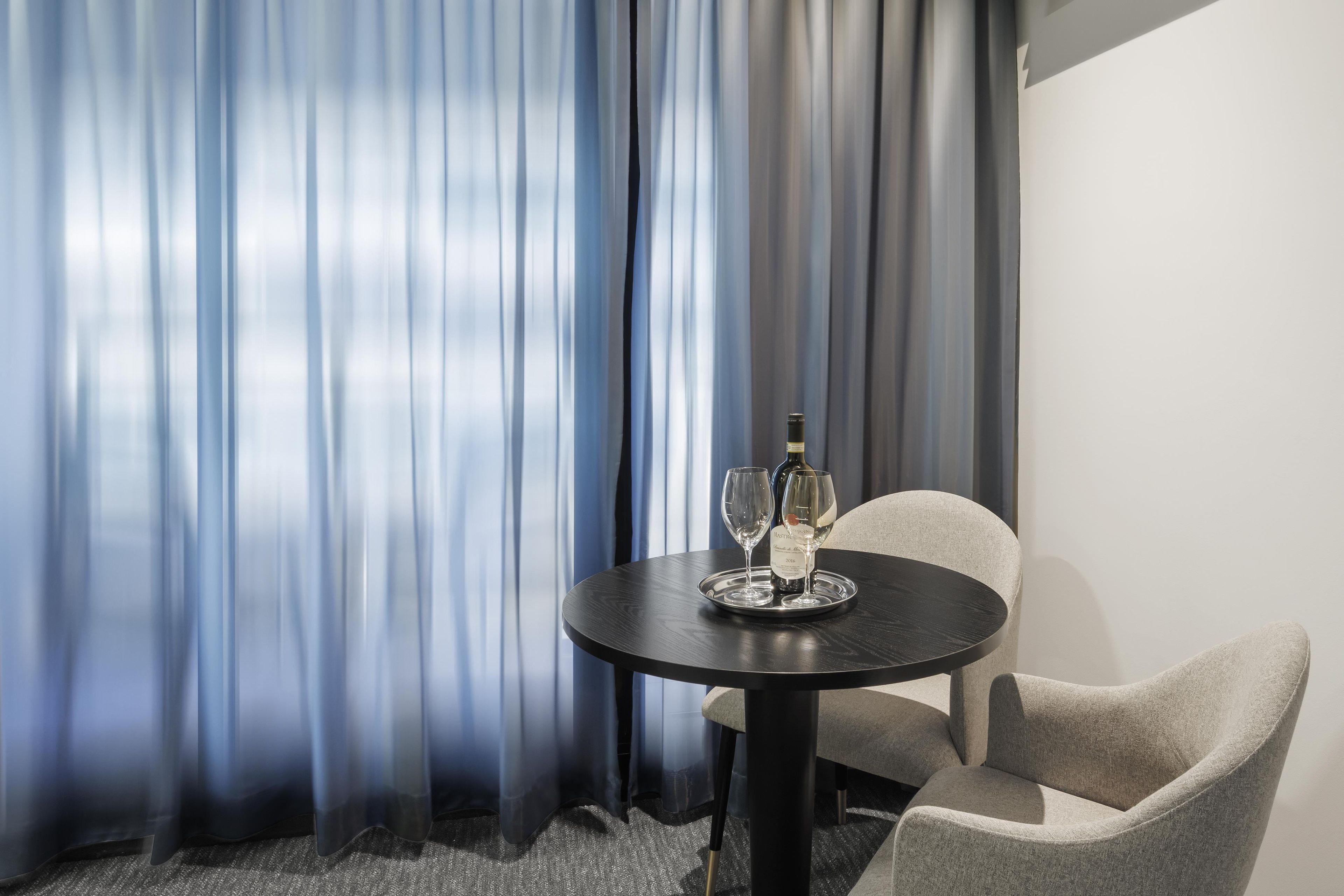 A hotel room with a round table, two wine glasses, and a bottle of wine.