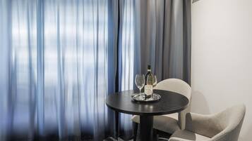 A hotel room with a round table, two wine glasses, and a bottle of wine.