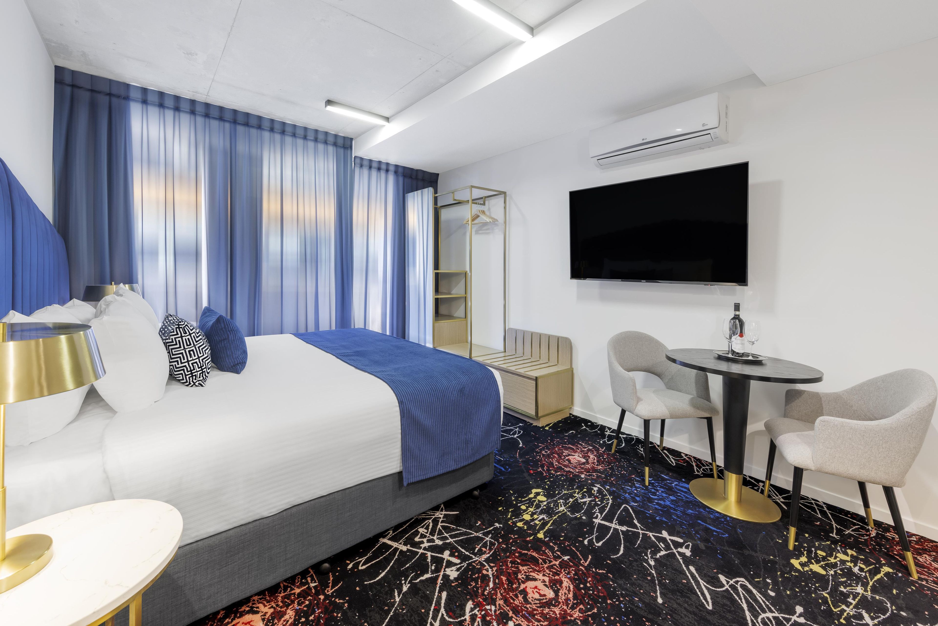 Une chambre d’hôtel comprenant un lit, un bureau, deux chaises, une télévision et une armoire.