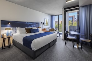 A hotel room with a large bed, a desk, and a chair. There is a window with a view of buildings and trees. - Oaks Melbourne St Kilda Road Hotel (Melbourne)