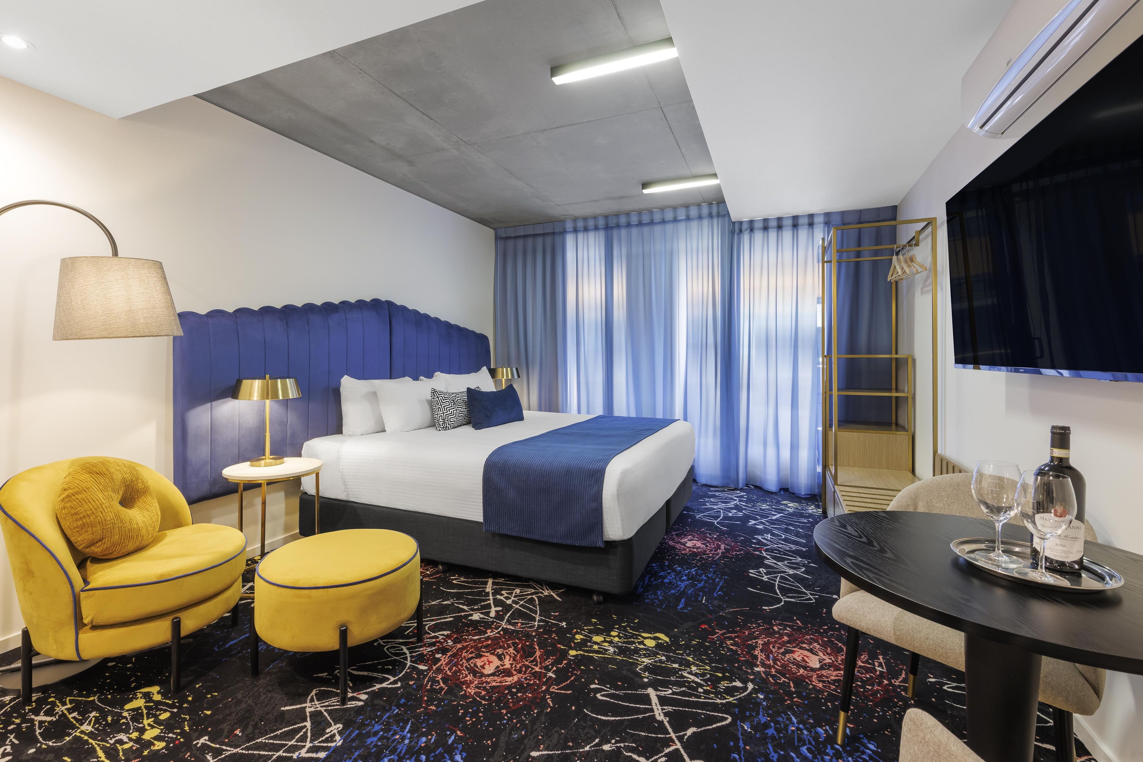Una habitación de hotel con cama, escritorio, silla, lámpara y televisión.