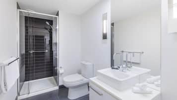 Uma casa de banho moderna com cabine de duche em vidro, sanita e lavatório branco com espelho em cima.