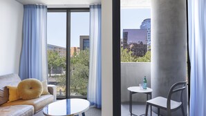 Ein modernes Zimmer mit einer Couch, einem runden Tisch und einem Balkon mit Blick auf Gebäude und Bäume.