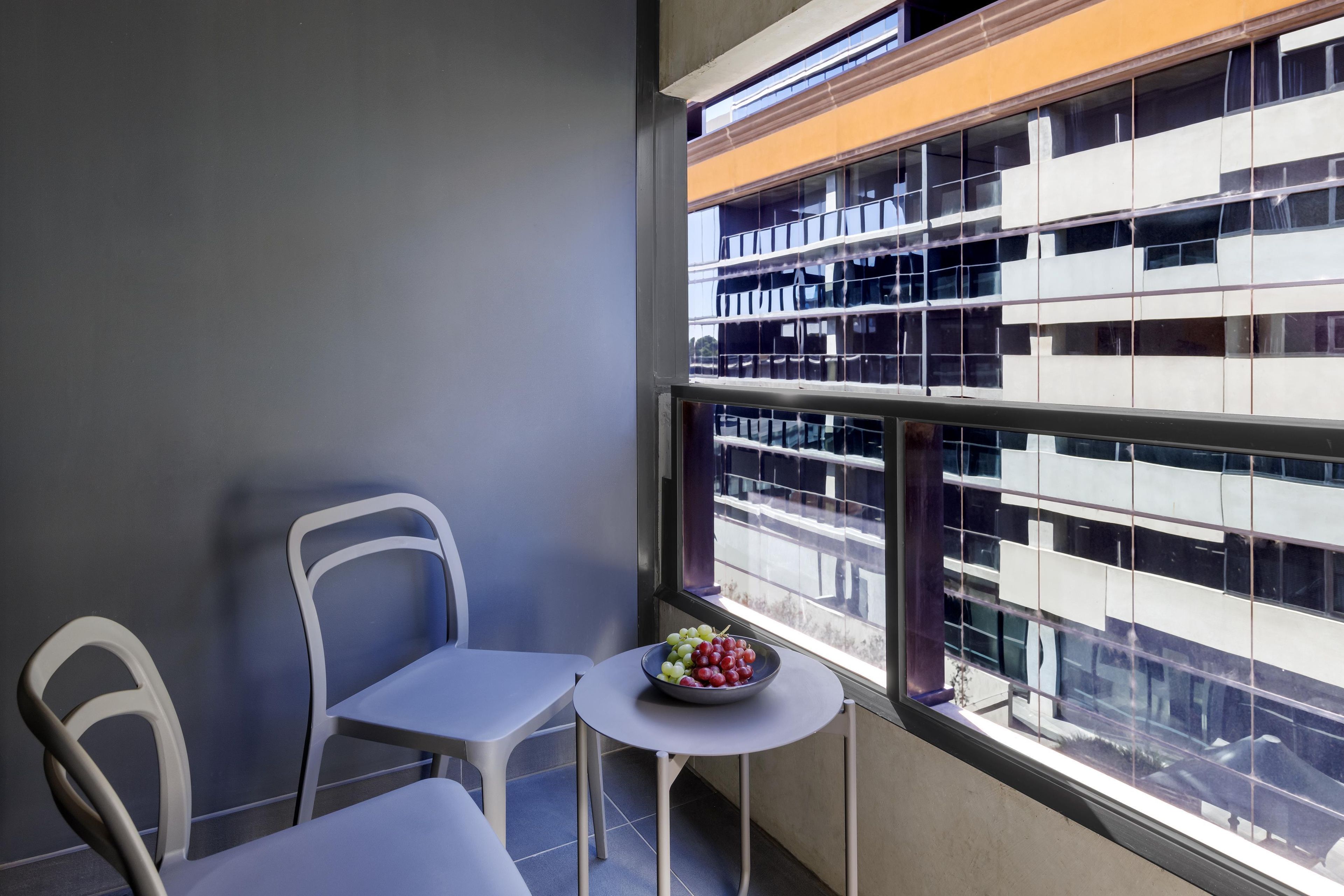 Un balcone con vista su un edificio, un tavolino con una ciotola di frutta e due sedie.