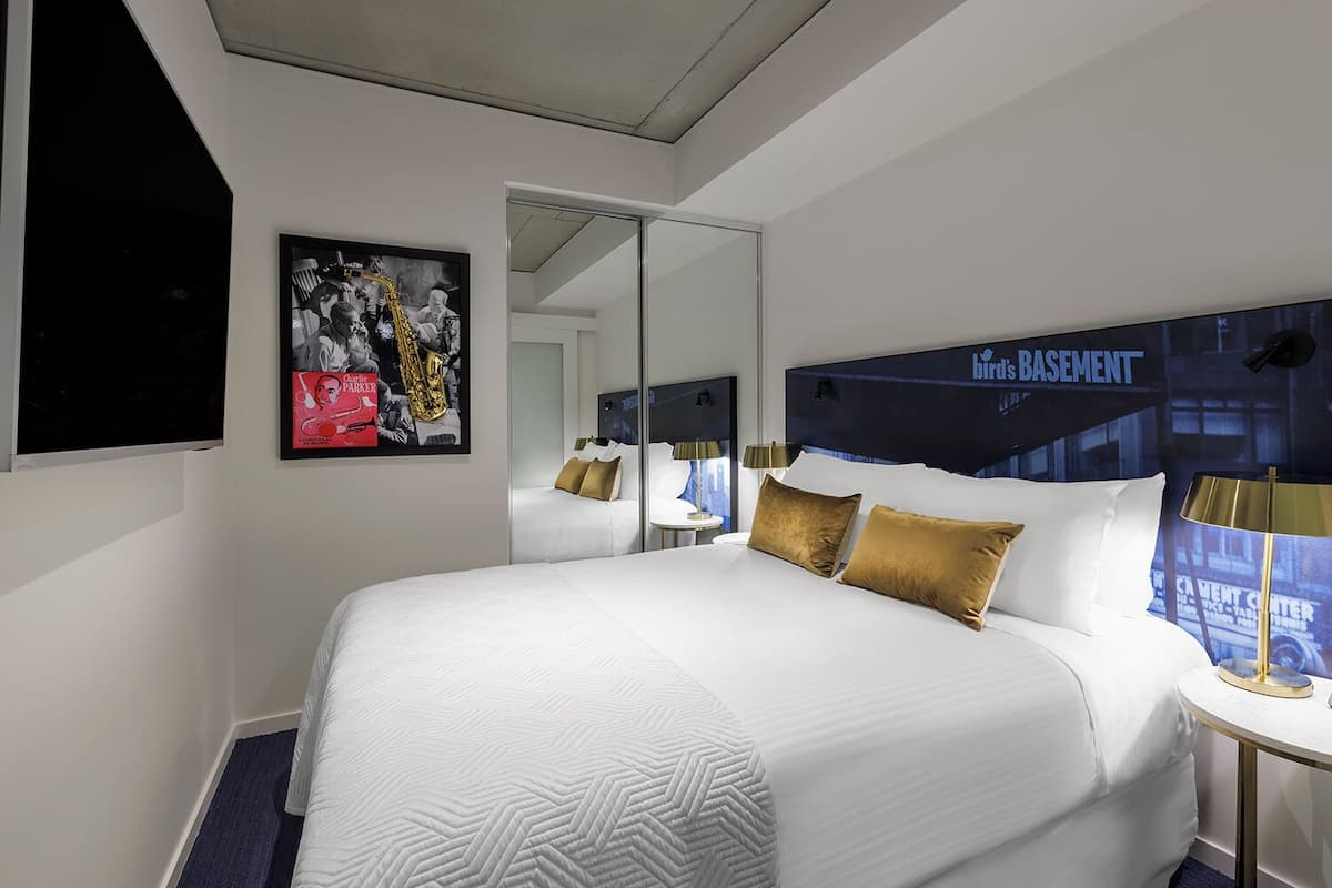 A hotel room with a large bed, a mirror, a framed poster, and a sign indicating the basement.