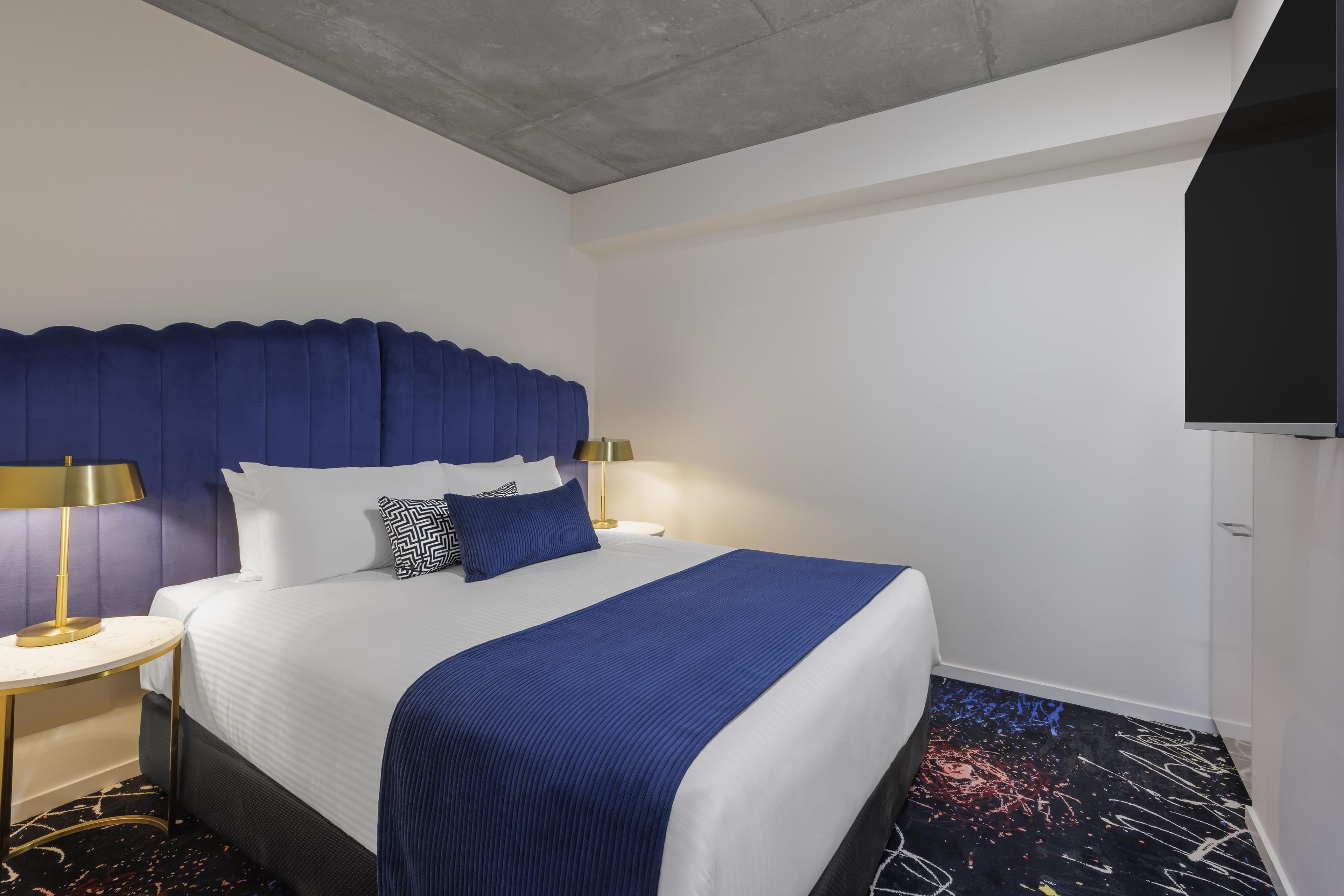 Een hotelkamer met een bed, nachtkastje, lamp en televisie.