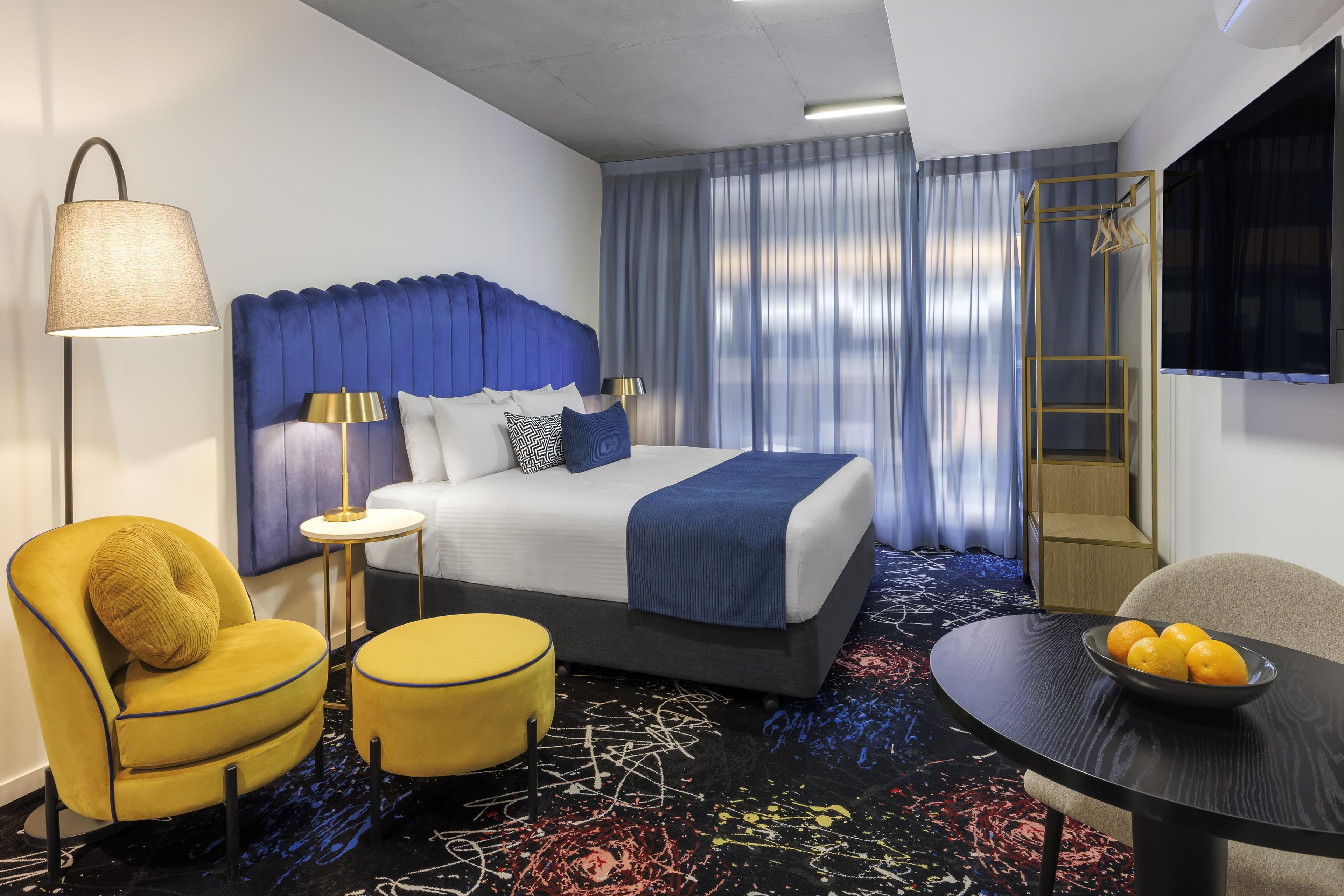 A hotel room with a bed, a desk, a chair, a lamp, and a television.
