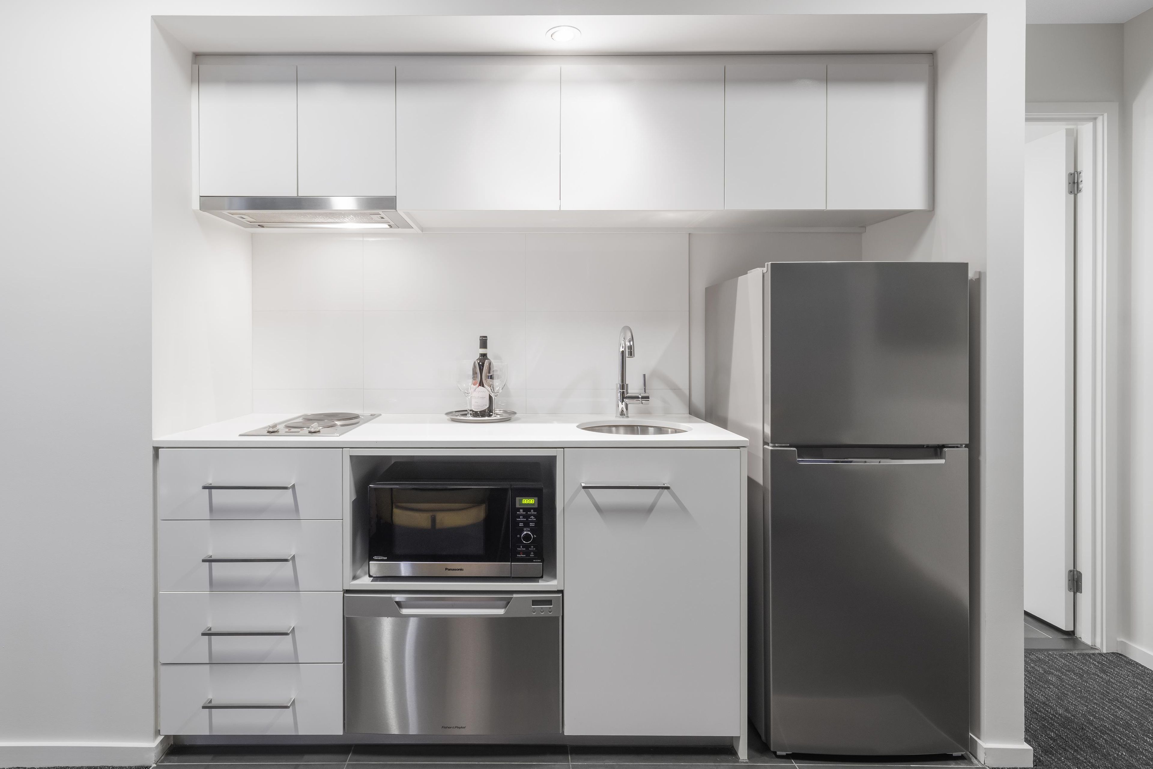 A compact kitchen with a built-in microwave, dishwasher, and a stainless steel refrigerator.