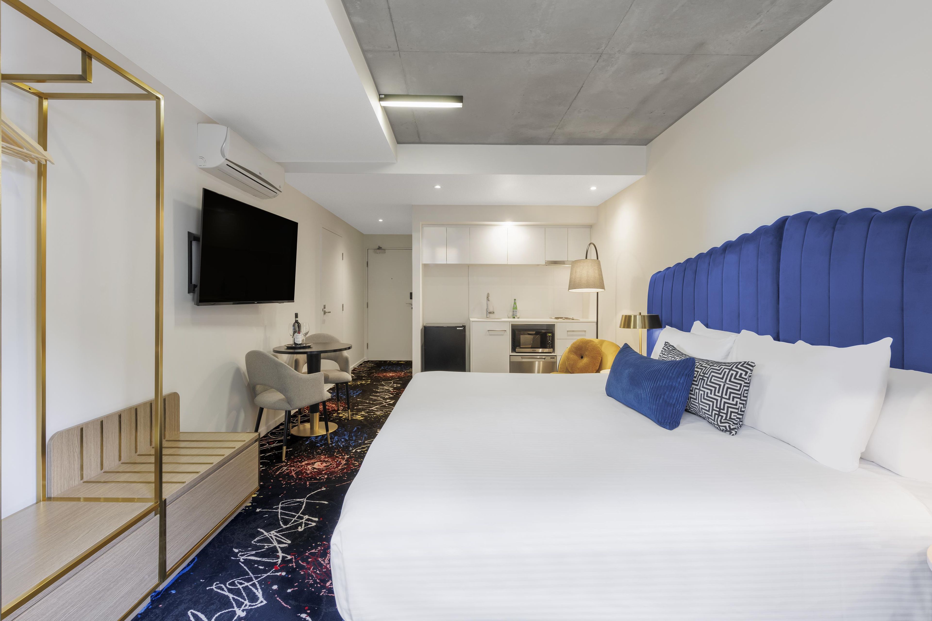Habitación de hotel con una cama grande, televisión de pantalla plana, una pequeña cocina y un área de descanso con mesa y sillas.