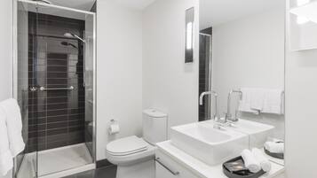 Un baño moderno con ducha envuelta en vidrio, inodoro y tocador con lavamanos y espejo.
