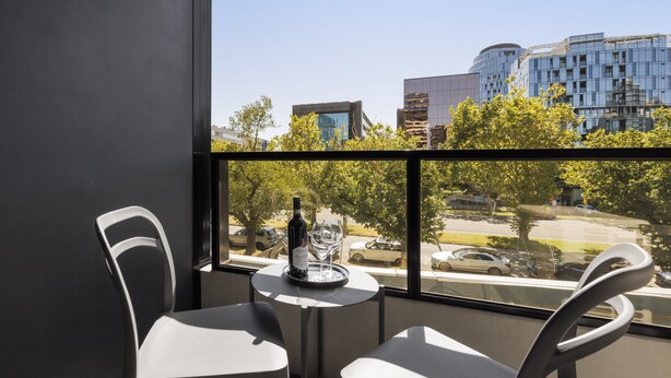 Ein Balkon mit zwei weißen Stühlen und einem Tisch, einer Weinflasche und einem Glas auf dem Tisch.
