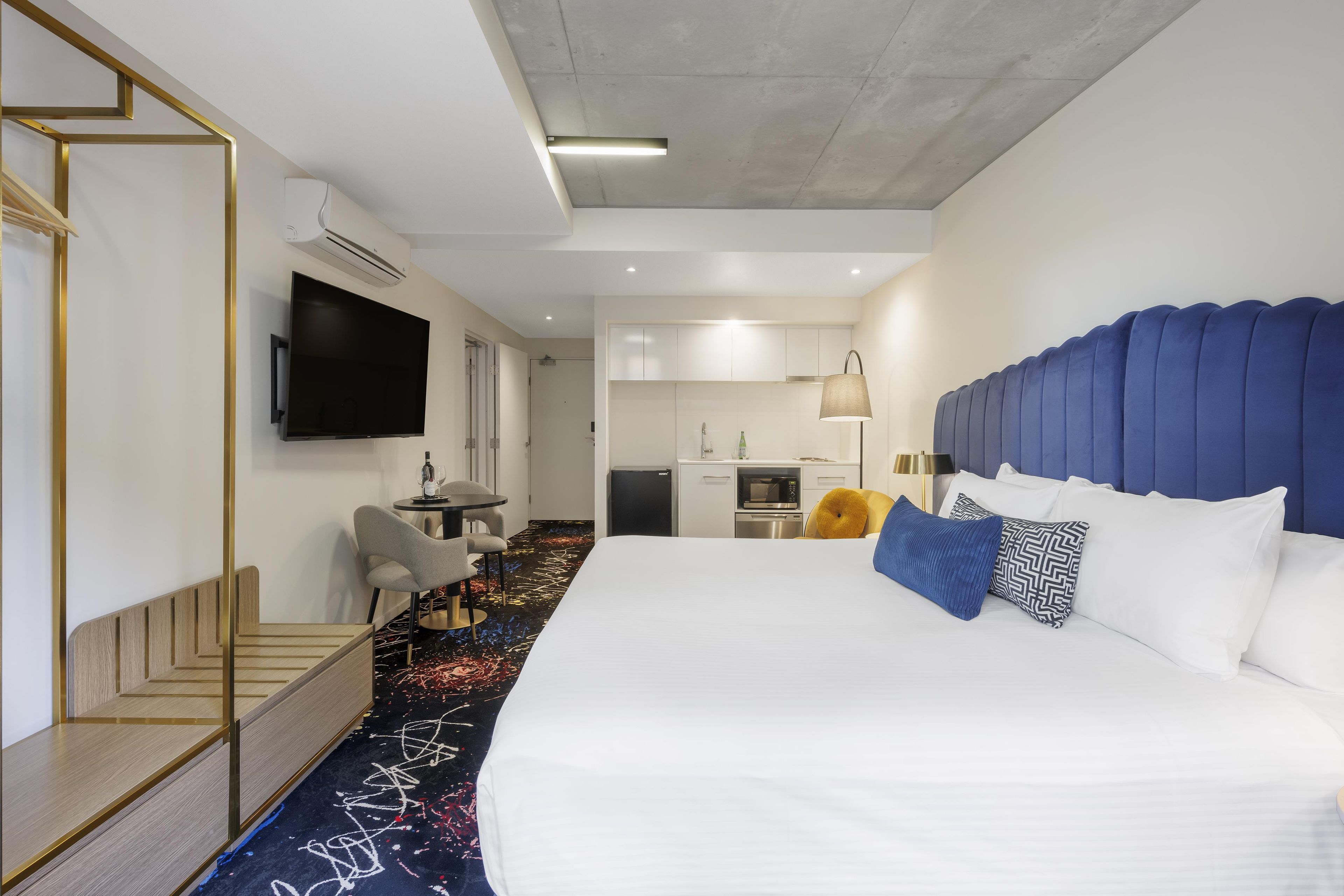 Ein Hotelzimmer mit einem großen Bett, einem Flachbildfernseher, einem Schreibtisch mit Stuhl, einer kleinen Küchenzeile und einem Badezimmer.