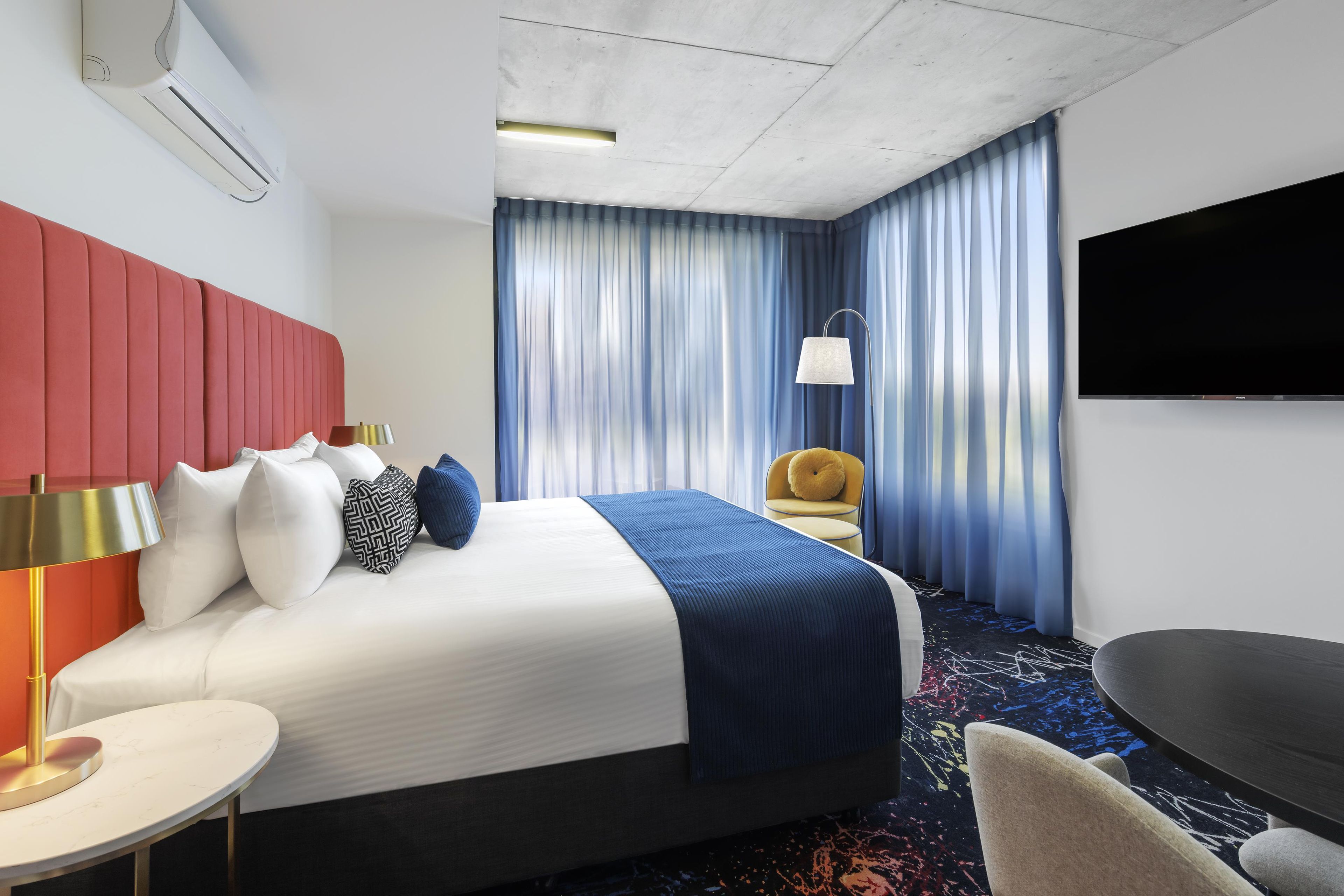 Une chambre d’hôtel avec un lit, un bureau, une chaise, une télévision et une fenêtre avec des rideaux.
