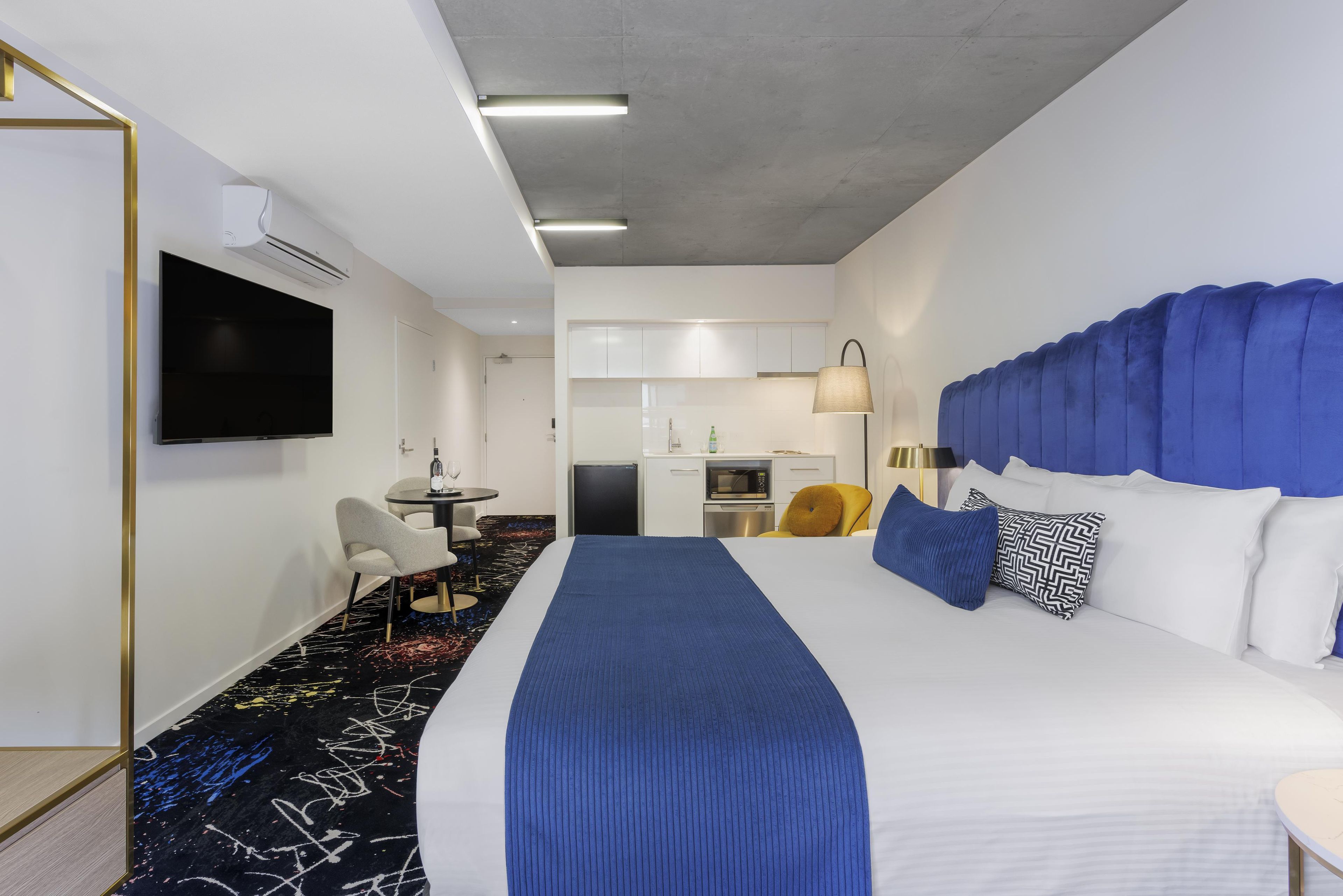 Habitación de hotel con una cama grande, televisión de pantalla plana, escritorio con silla, microondas y pequeña kitchenette.