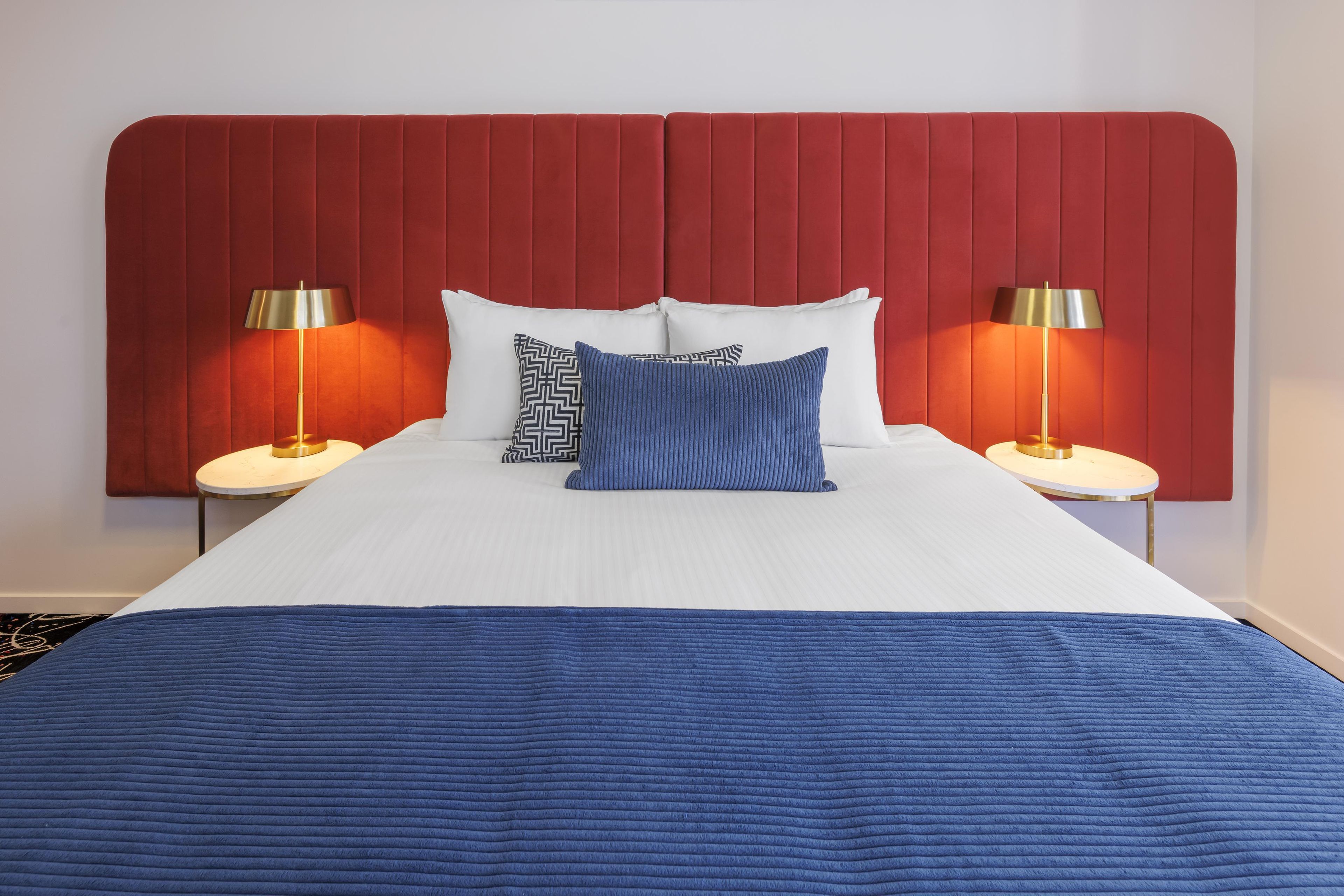 Une chambre d’hôtel avec un grand lit, deux lampes de chevet et une tête de lit rouge.