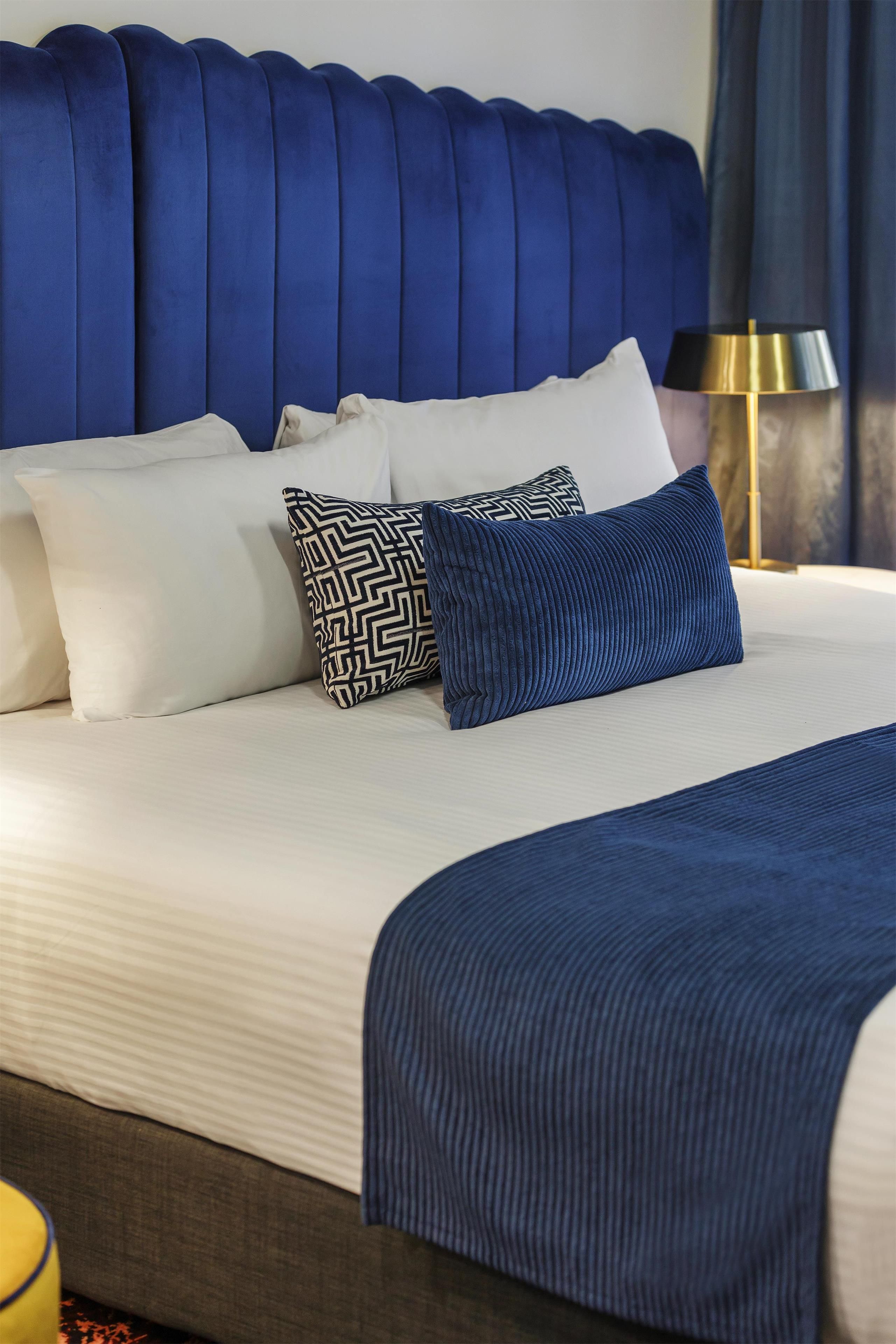 Habitación de hotel con una cama grande, varios almohadones, una lámpara de noche y vistas al exterior.
