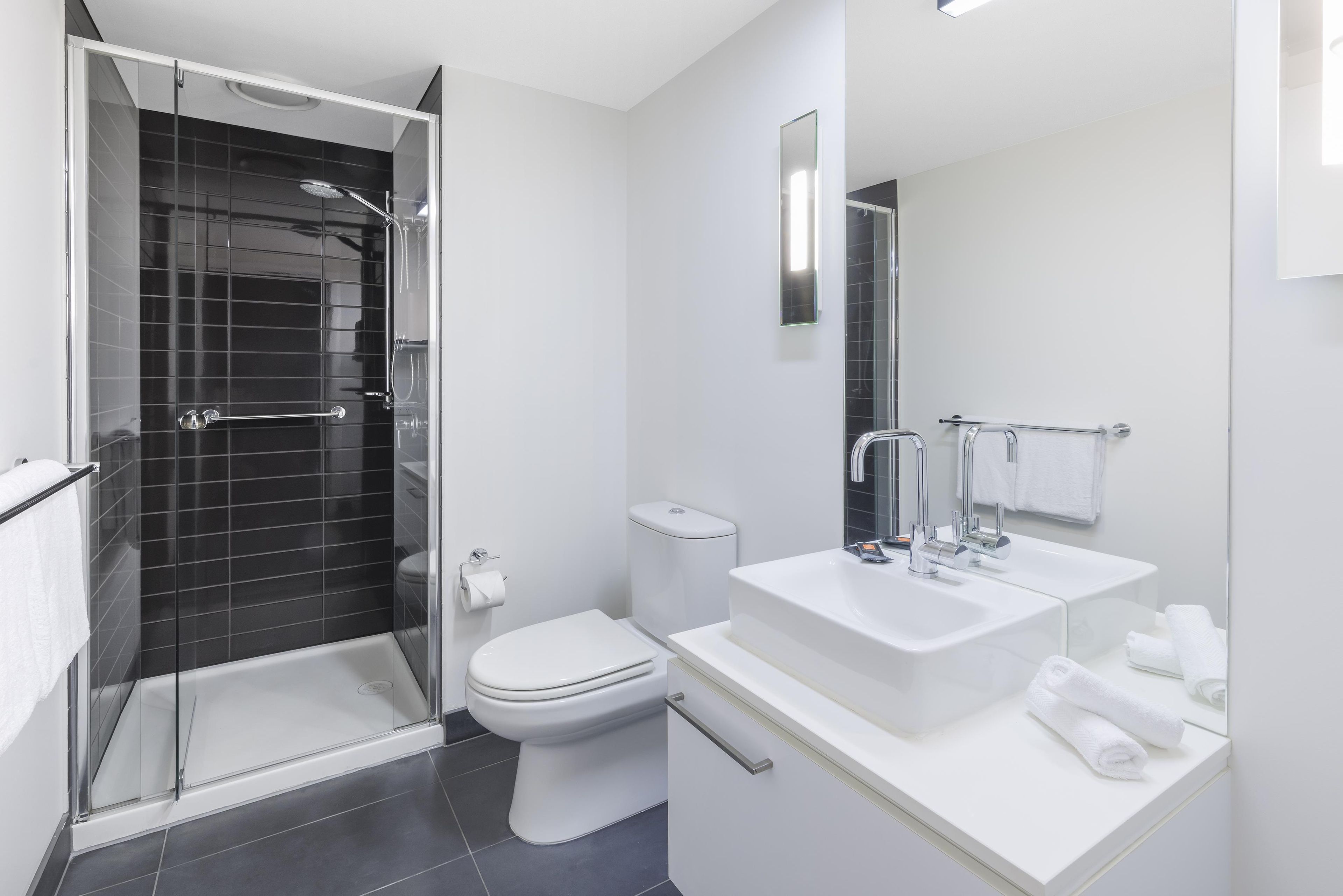 Un bagno moderno con doccia vetro, un water e un lavandino con specchio.