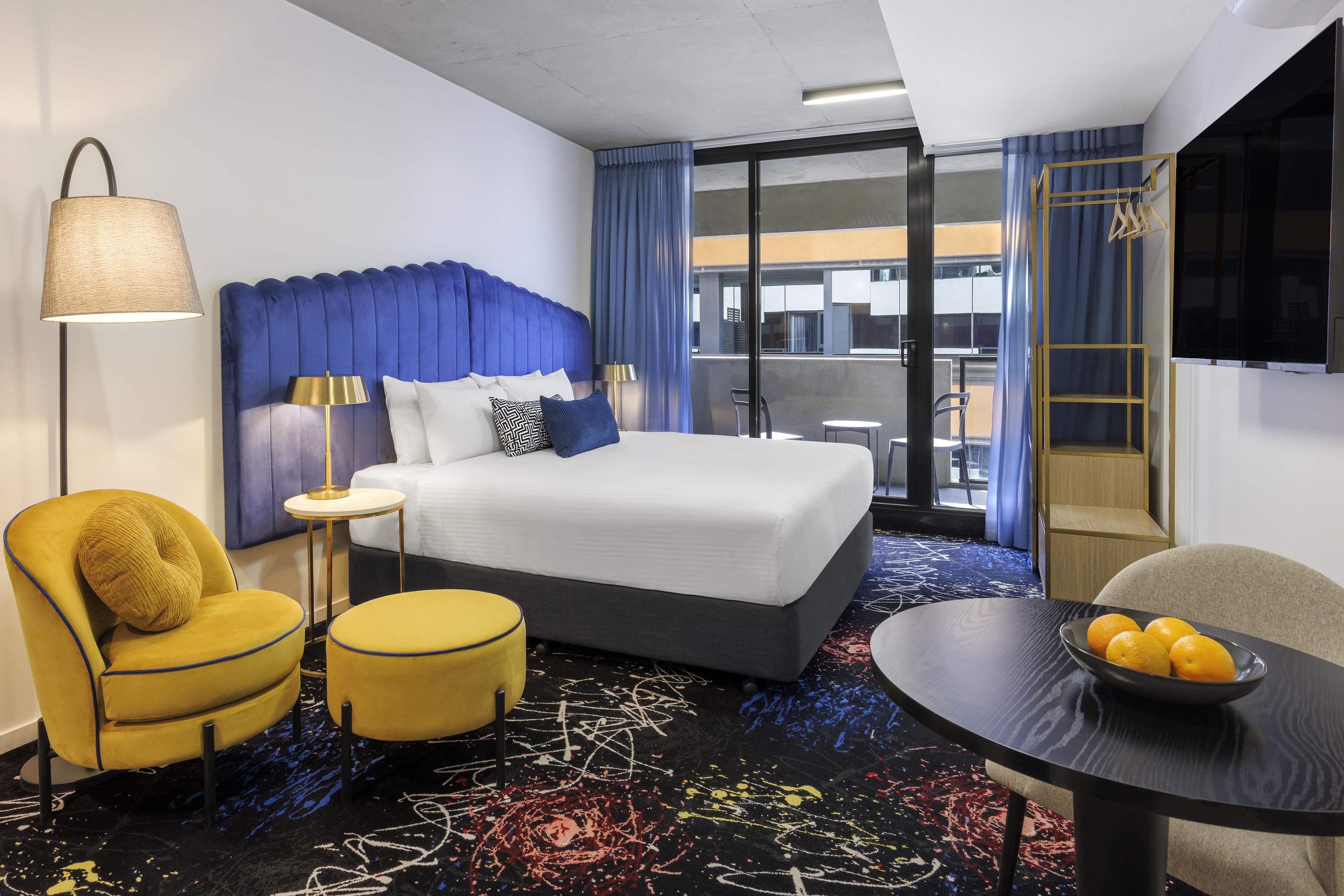 Una habitación de hotel con cama, escritorio, silla, lámpara y televisión.